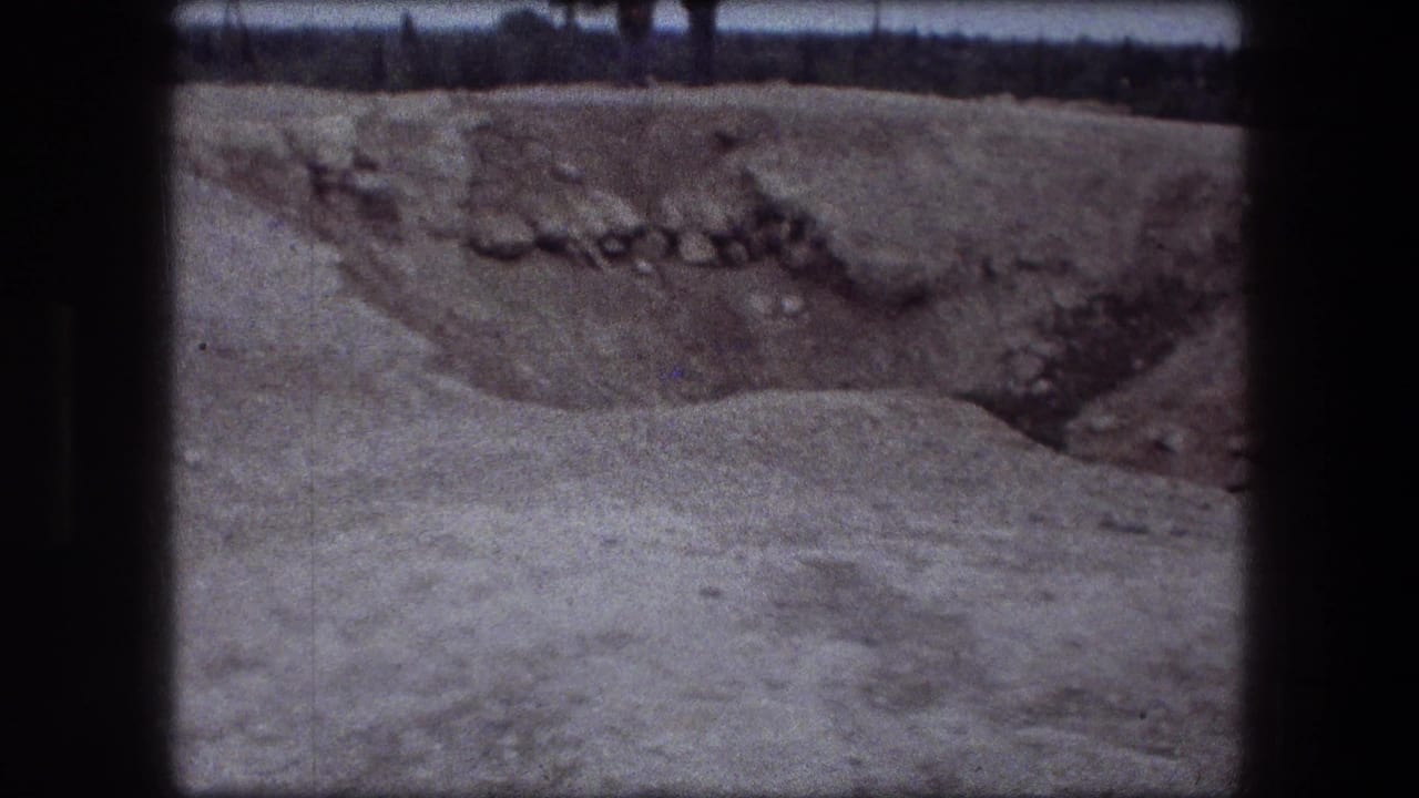 Dark-bordered 8mm frame showing a gray dirt or terrain surface with a darker depression near the top.