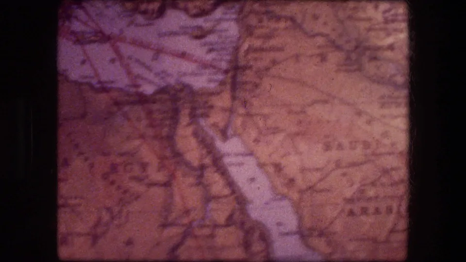 Close-up of a folded paper map in 1976 8mm footage, with partly legible regional labels and light-toned highlighted shapes.