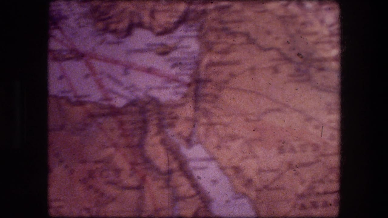 A second 1976 8mm frame holds on the weathered map-like surface, with soft focus, color fading, and black film edges.