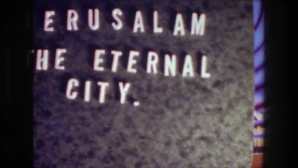 8mm frame of the Jerusalem title card, showing white letters, dark surface texture, grain, and a purple edge tint.