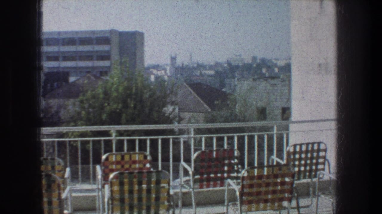 Checkered lawn chairs on a balcony overlooking rooftops and a distant building.