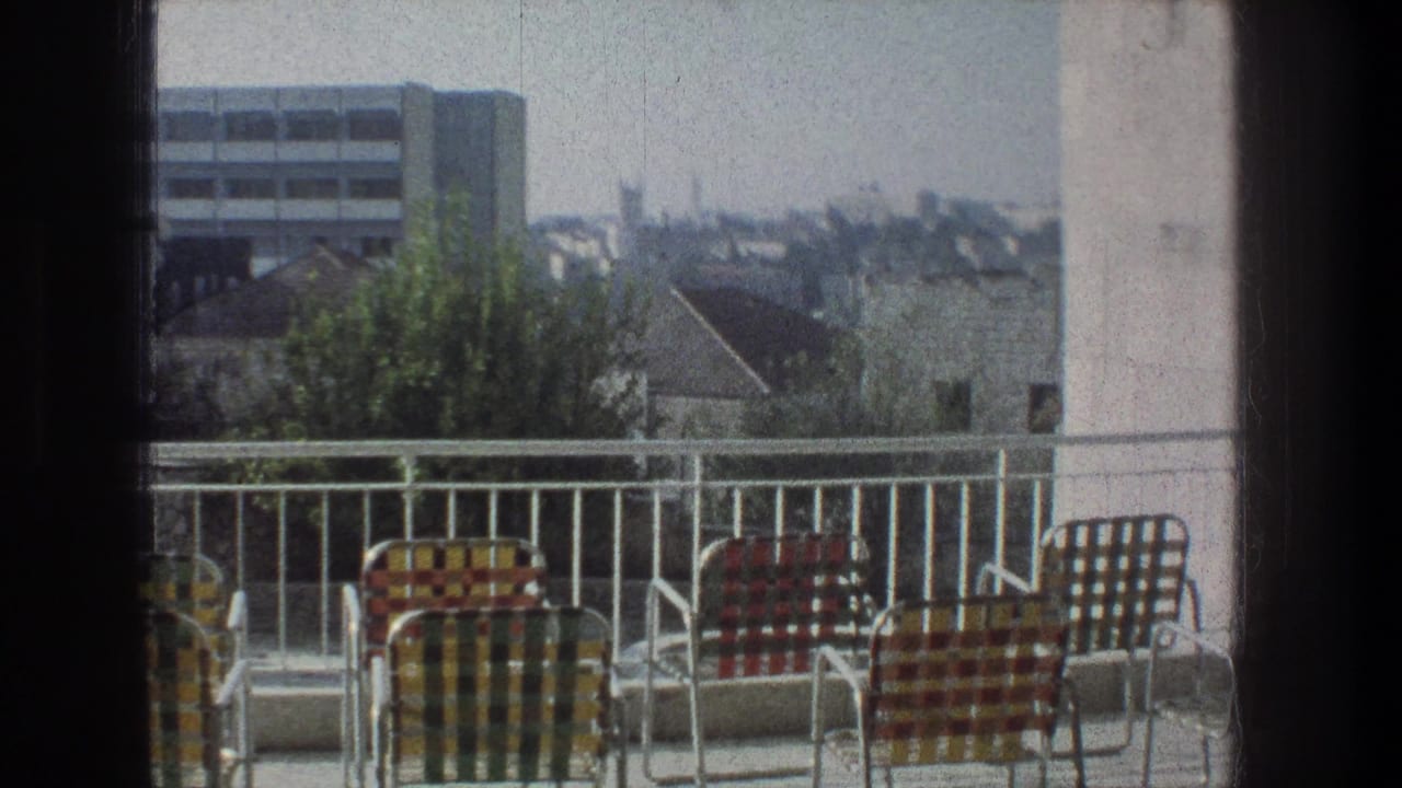 1976 Jerusalem home-movie frame showing colorful lawn chairs on a balcony with rooftops, trees, and a distant modern building.