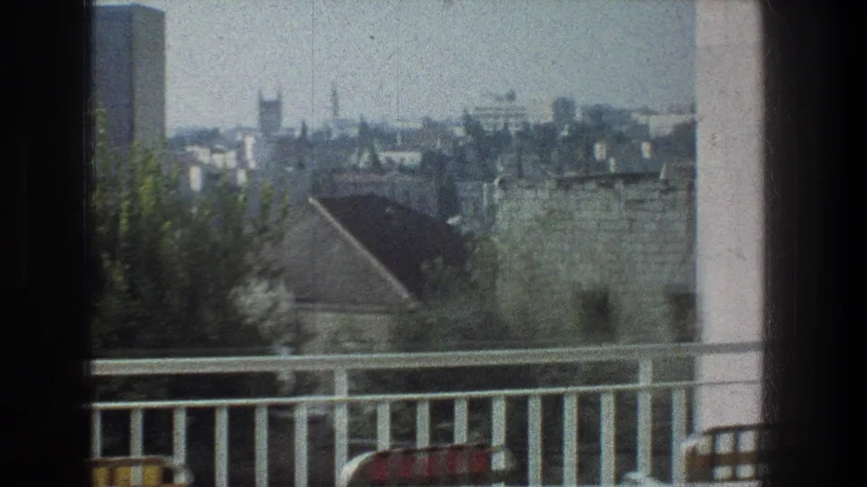 Late-frame 1976 Jerusalem balcony shot with the railing low in frame, rooftops and trees beyond, and a hazy city distance.
