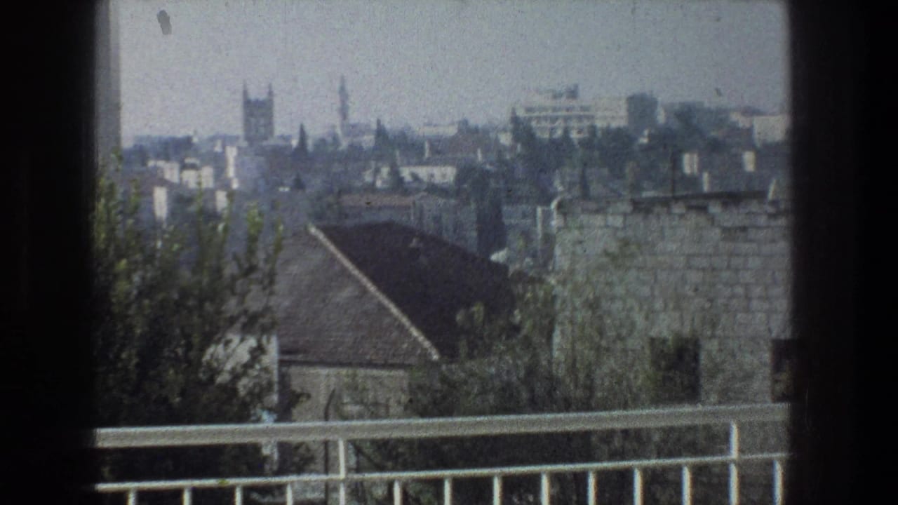 Hazy elevated view over Jerusalem rooftops with trees and a balcony rail in the foreground.
