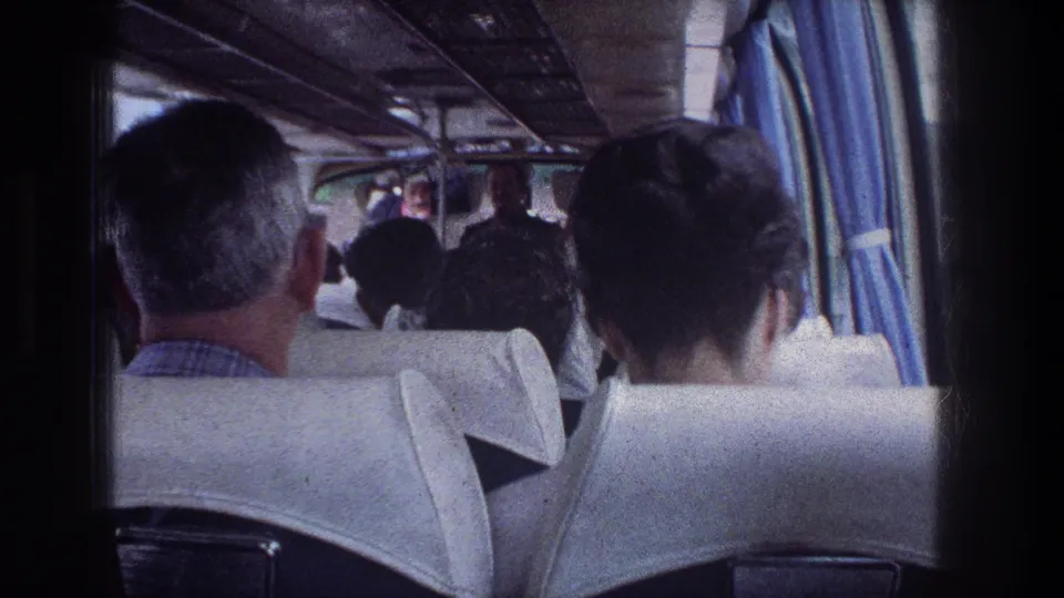 Seated passengers inside a 1976 Jerusalem bus, with the camera looking forward past white seats and blue window curtains.