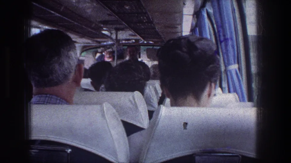 Rear view inside a crowded 1976 Jerusalem travel bus, with seated adult passengers, white seat covers, and blue curtains along the windows.