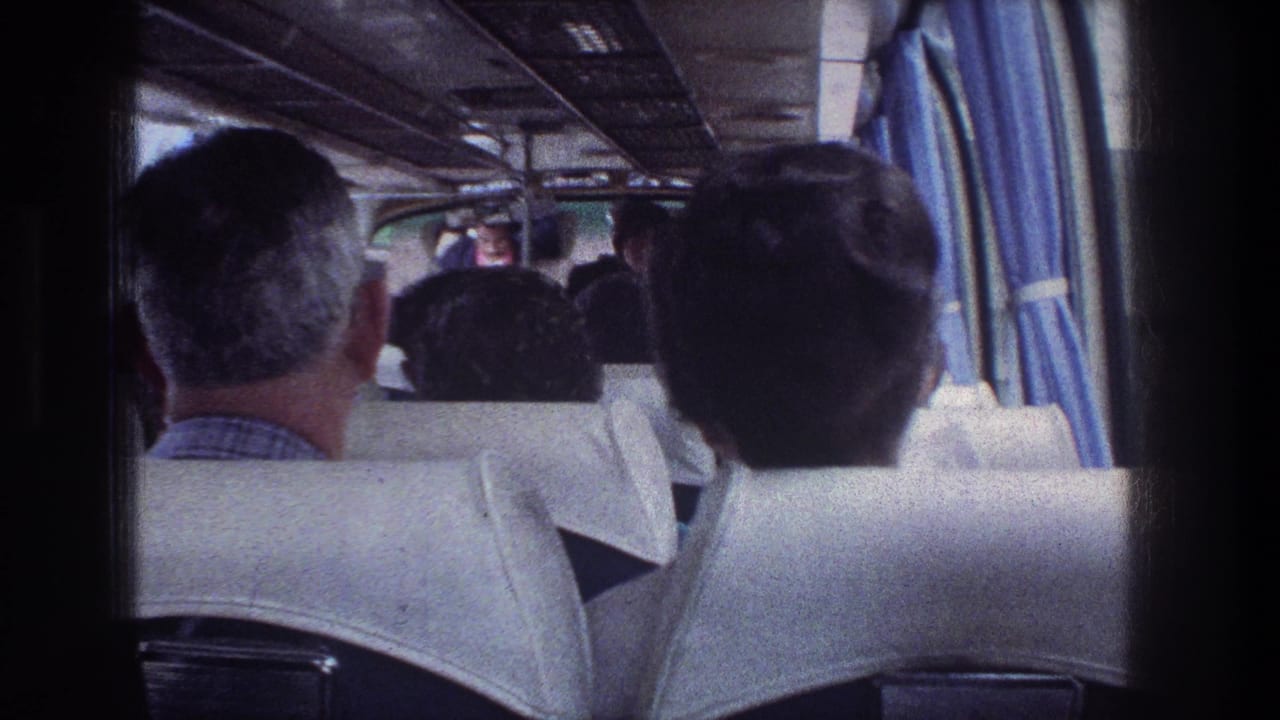 Rear bus view with seated passengers, curtains, and the aisle leading forward.