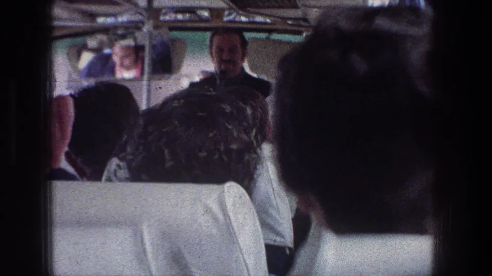 A guide or speaker stands near the front of a crowded 1976 Jerusalem bus as passengers watch from white-upholstered seats.