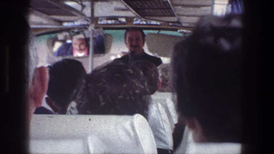 1976 Jerusalem tour-bus interior with seated passengers facing a guide at the front of the aisle.