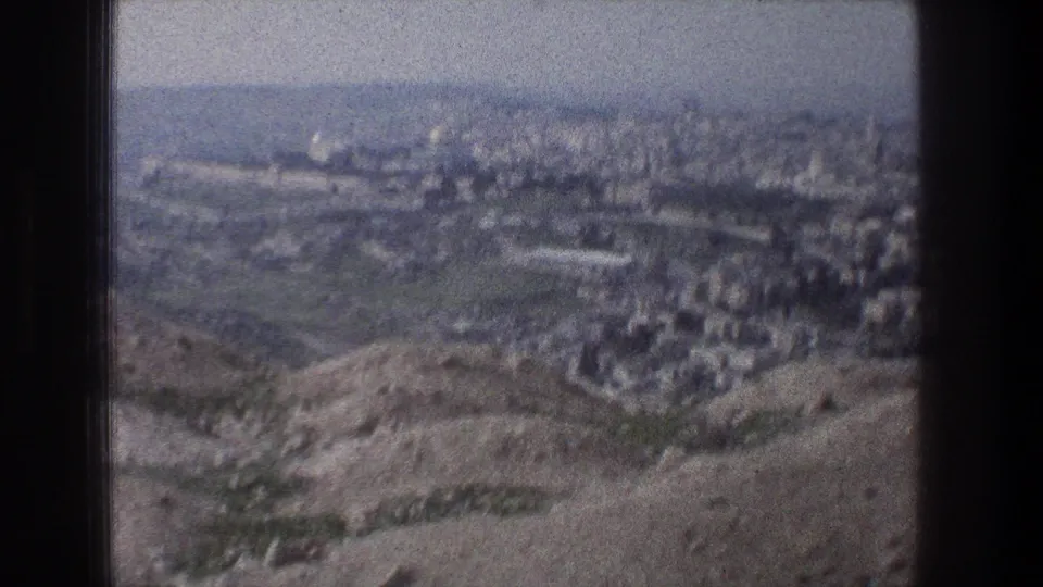 A panoramic Jerusalem city view appears beyond rocky hills, filmed through a bus window on 8mm in 1976.