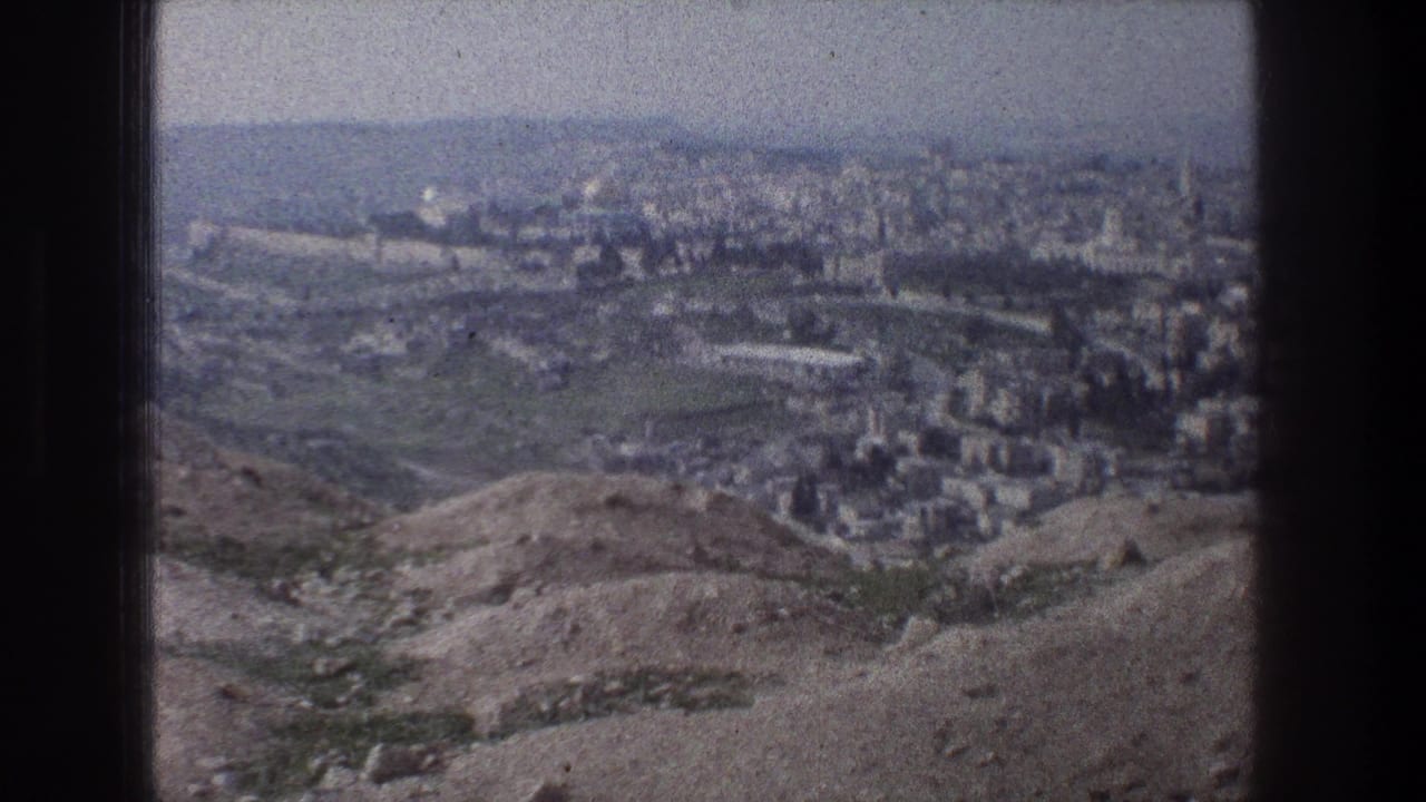 1976 8mm view from a Jerusalem hilltop, looking over arid slopes toward clustered pale buildings and a distant skyline.