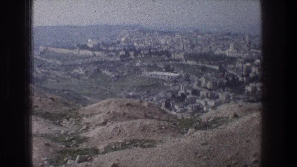 1976 8mm view from a Jerusalem hilltop, looking over arid slopes toward clustered pale buildings and a distant skyline.