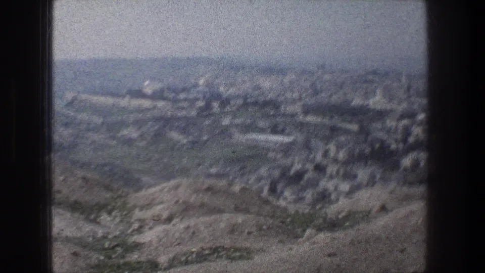 Jerusalem cityscape seen from above on 8mm film, with arid hills in front and pale urban blocks stretching across the valley.