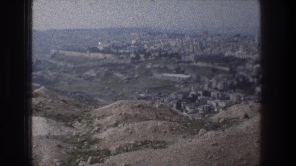 Jerusalem hilltop view on 8mm film, with rocky foreground, clustered buildings, and a distant domed landmark that appears to be visible.