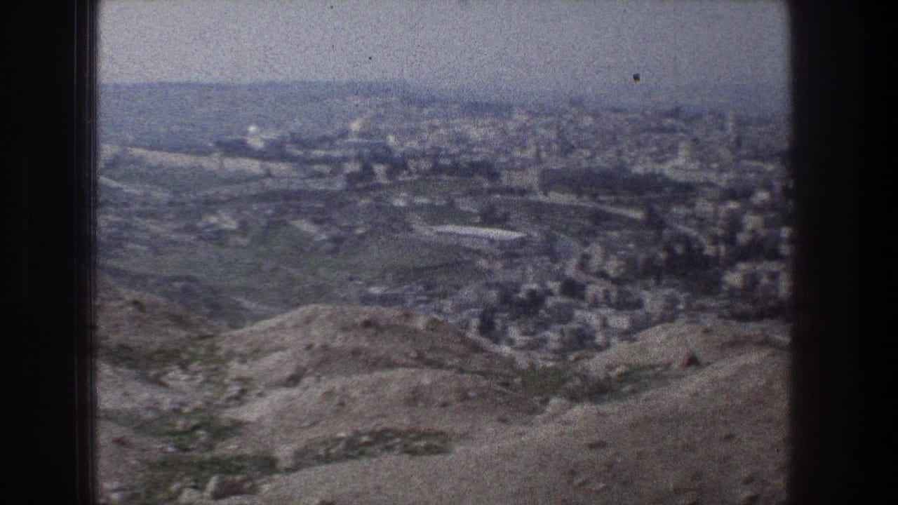 1976 8mm view over Jerusalem from a hillside overlook, with rocky foreground slopes and dense buildings in the distance.