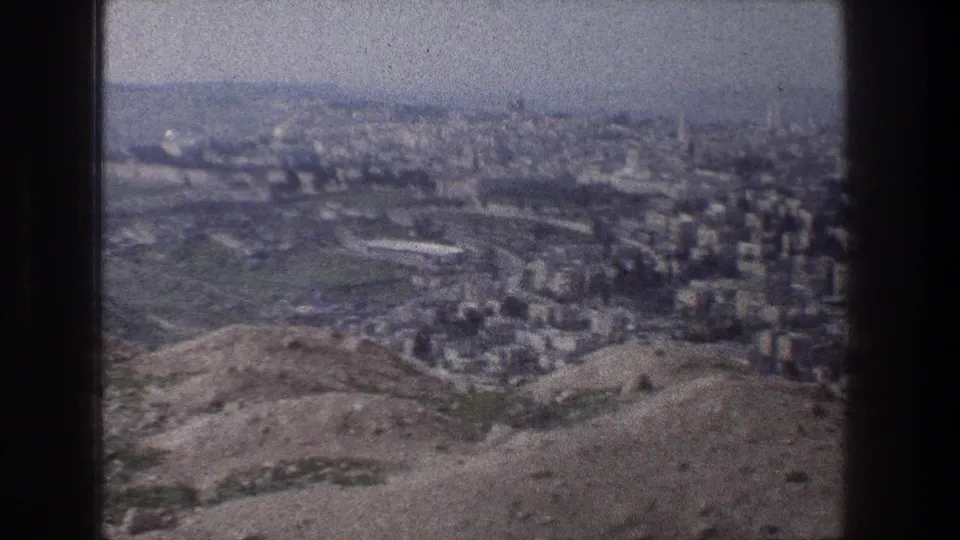Elevated 8mm frame of Jerusalem in 1976, showing open hillside terrain in front of dense city blocks and distant haze.