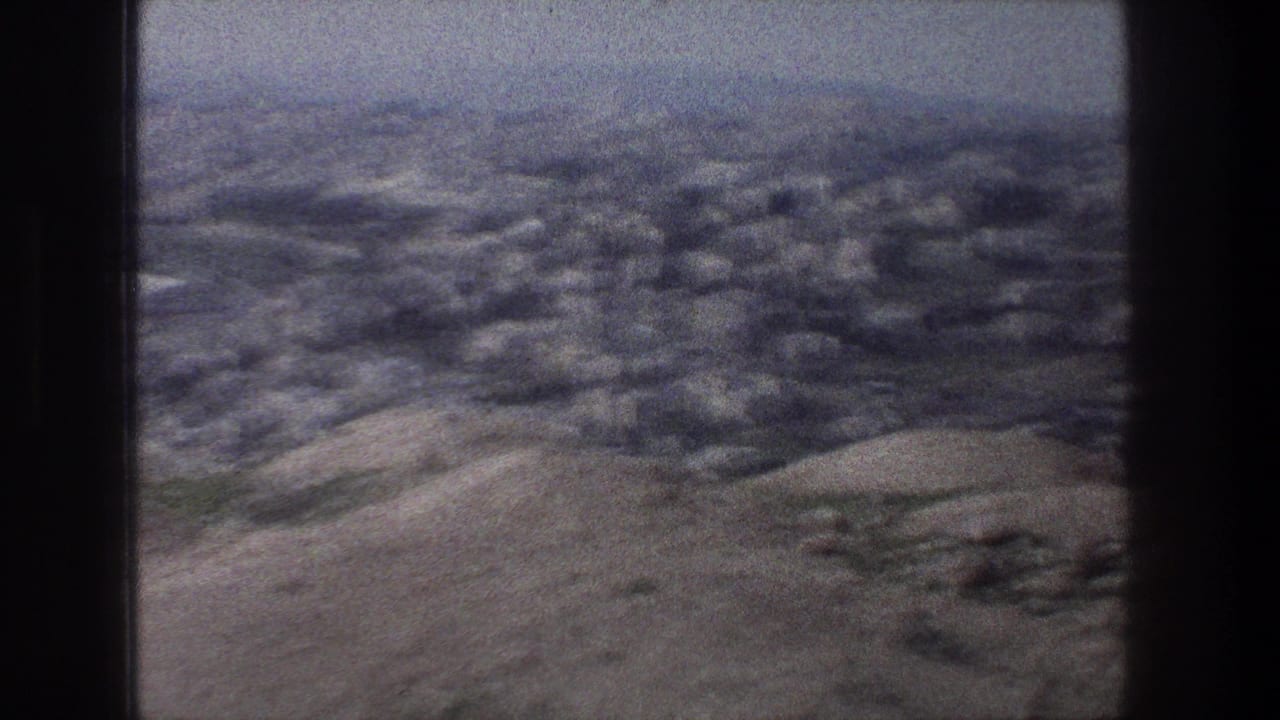 1976 8mm view over Jerusalem, showing pale buildings beyond rocky hills under a hazy sky.