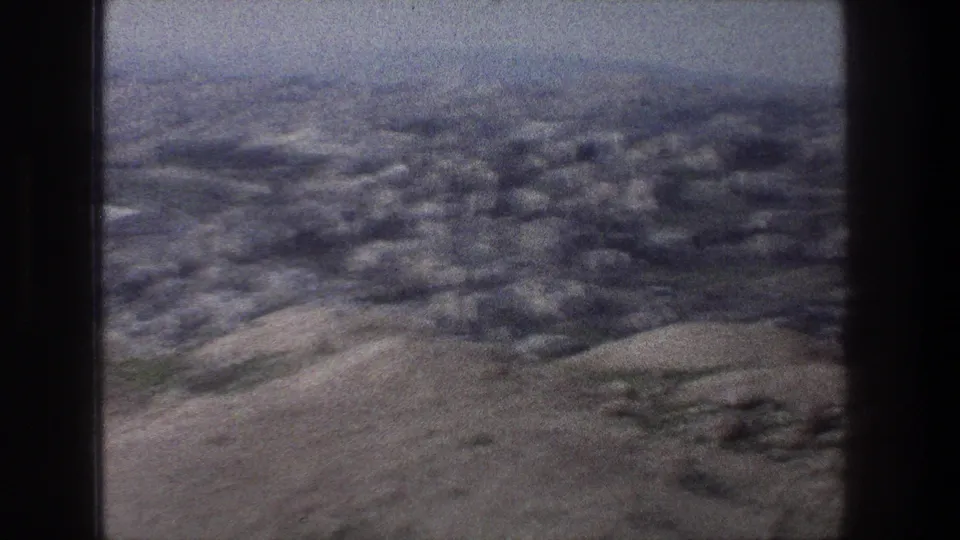1976 8mm view over Jerusalem, showing pale buildings beyond rocky hills under a hazy sky.
