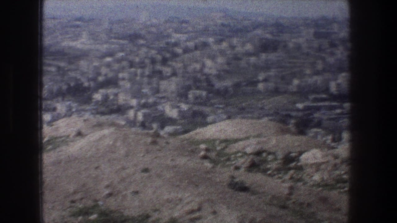 1976 home-movie frame of Jerusalem from above, with hilly terrain in front of a dense urban area.
