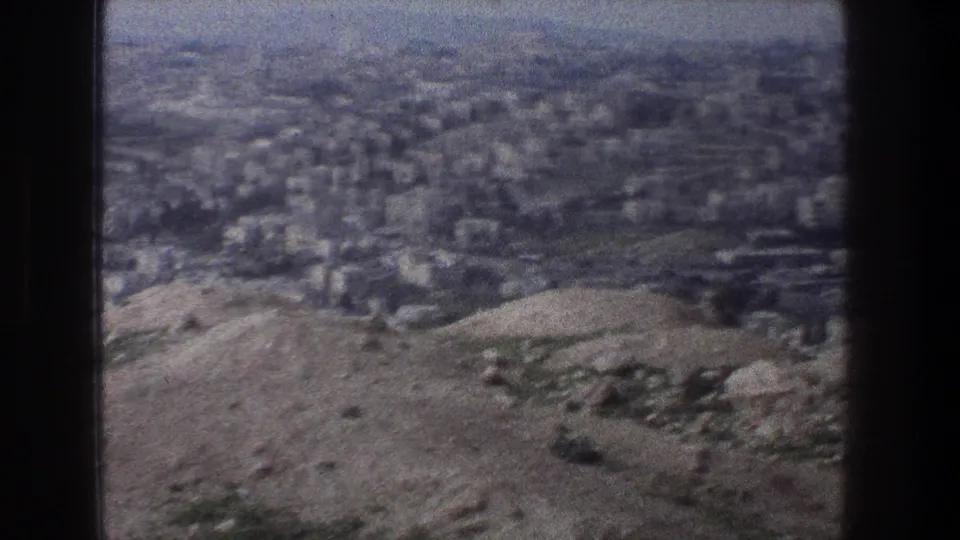 1976 home-movie frame of Jerusalem from above, with hilly terrain in front of a dense urban area.