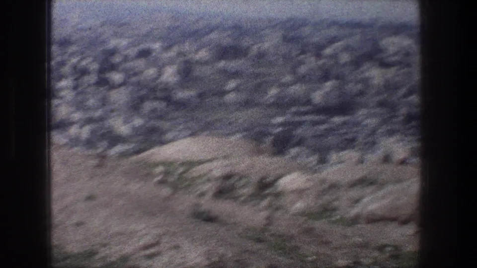 Soft 8mm frame from Jerusalem in 1976, looking past rocky hillside toward a hazy cityscape.