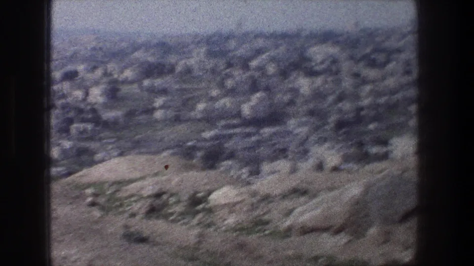 1976 8mm view of Jerusalem, with pale rocky slopes in the foreground and dense buildings beyond.