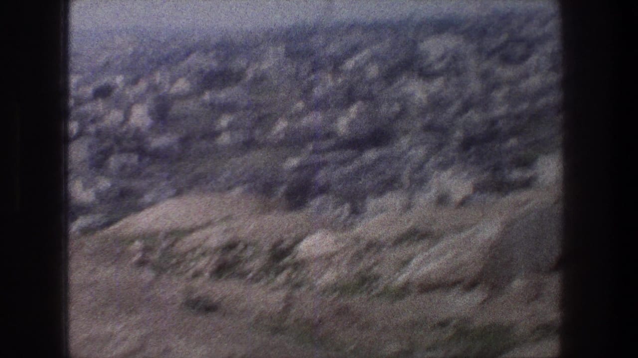 Soft 8mm frame of Jerusalem hillside terrain, with stone structures and sparse vegetation visible through motion blur.