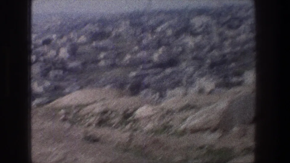 Soft 8mm frame of Jerusalem hillside terrain, with stone structures and sparse vegetation visible through motion blur.