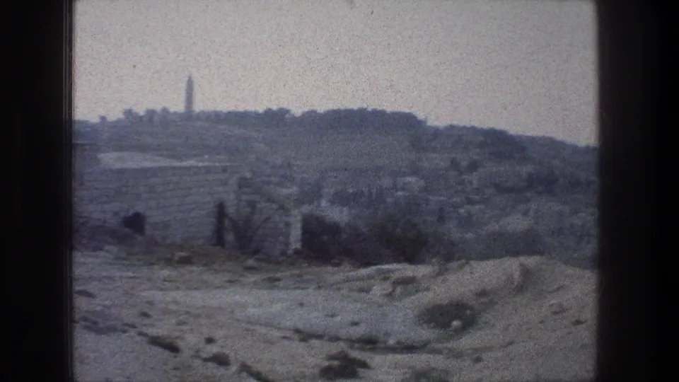 Closer 8mm view in Jerusalem showing a distant tower or obelisk on a ridge above low stone walls and arid foreground terrain.