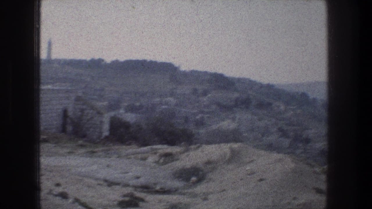 1976 8mm home-movie frame from Jerusalem showing gray rocky hills, scattered vegetation, and a slim vertical structure near the left horizon.