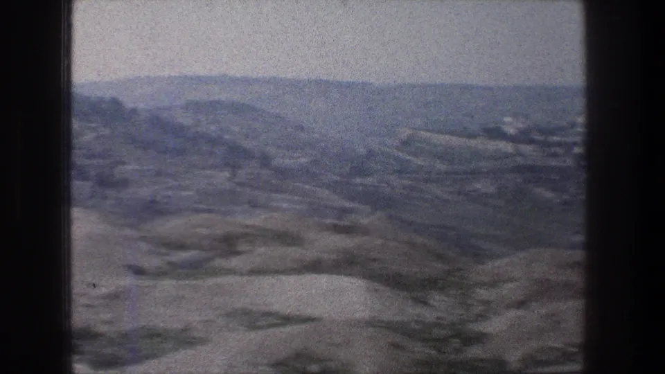 1976 Jerusalem home-movie frame showing a broad hillside panorama with layered ridges, pale slopes, and distant settlement patterns.