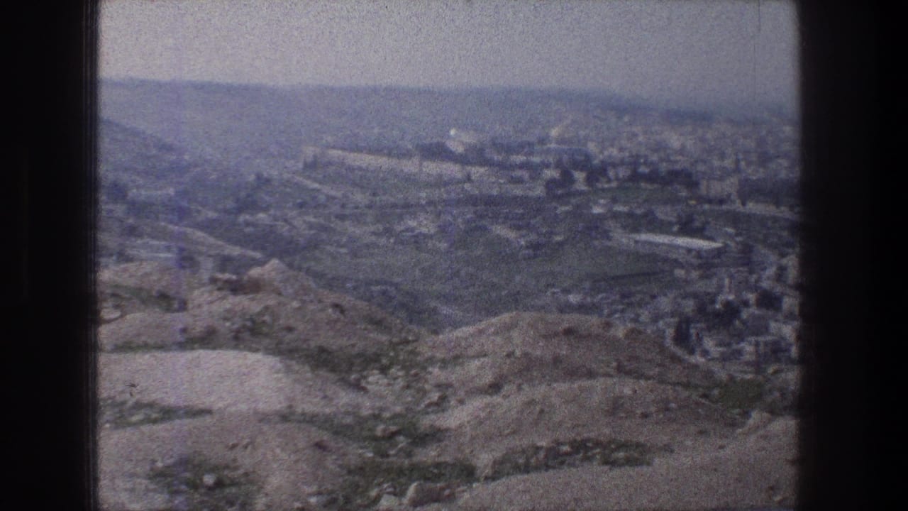 1976 8mm view of Jerusalem from a hilltop, with dry foreground slopes and a hazy distant urban skyline.