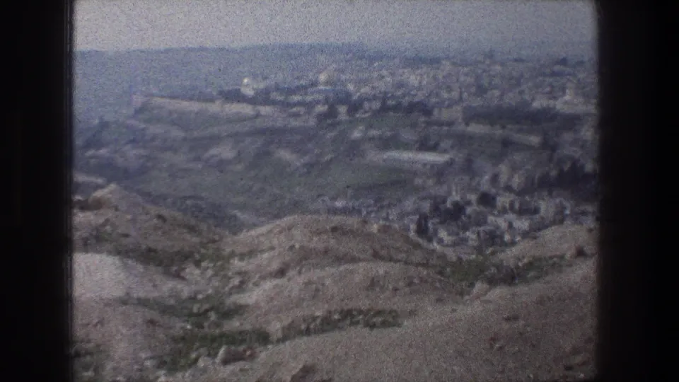 Jerusalem appears in the distance beyond dry hills, with a soft 8mm look and hazy blue-gray skyline.