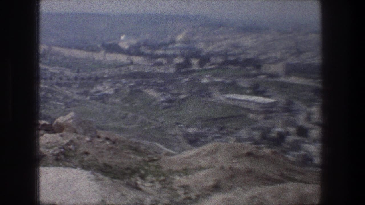 Soft 8mm view over rocky foreground, green hills, roads, and distant Jerusalem buildings.