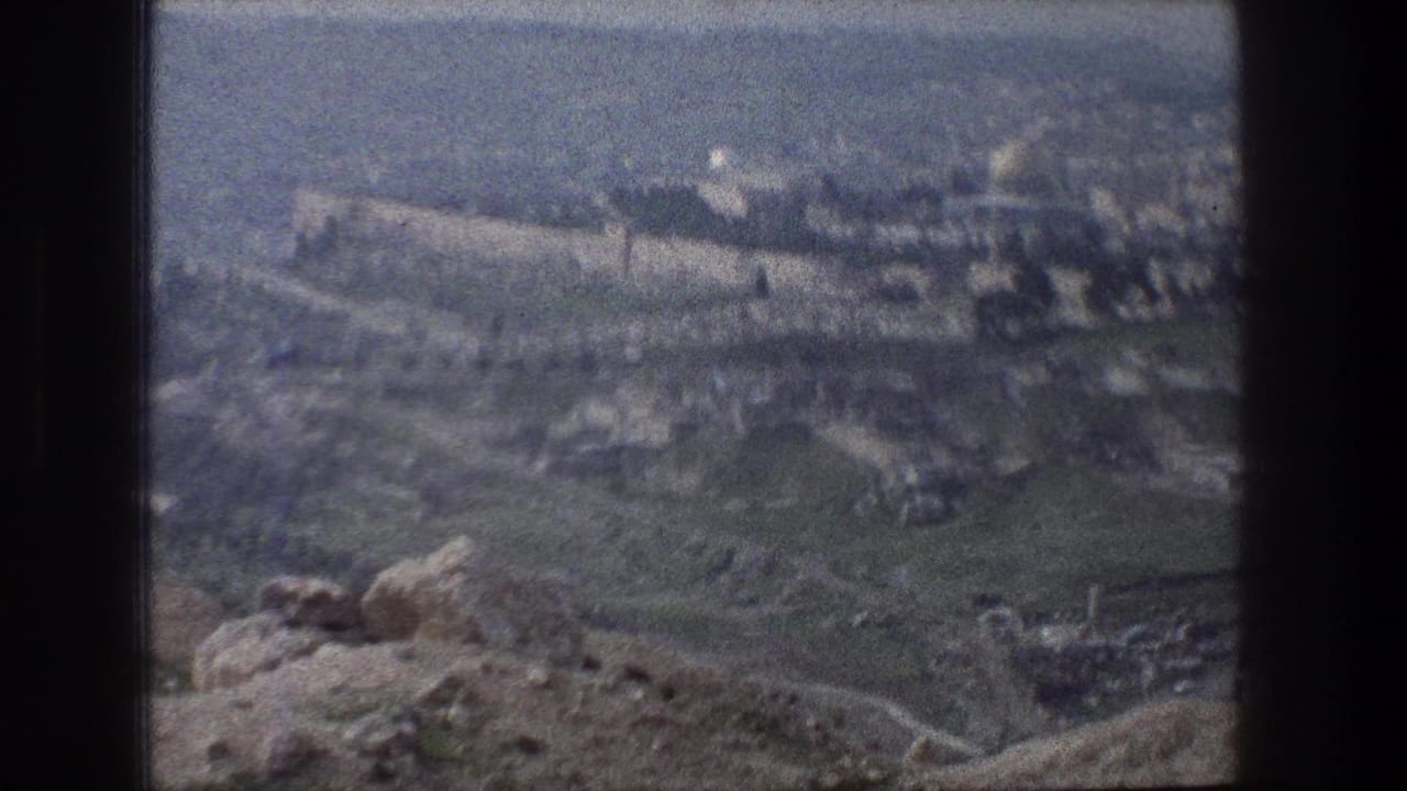 Distant city walls and domed landmark beyond green hillside and rocky overlook.