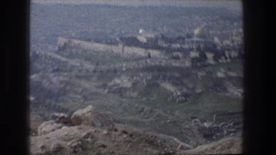1976 Jerusalem view with tan walls, a distant domed landmark, green slopes, and soft 8mm film grain.
