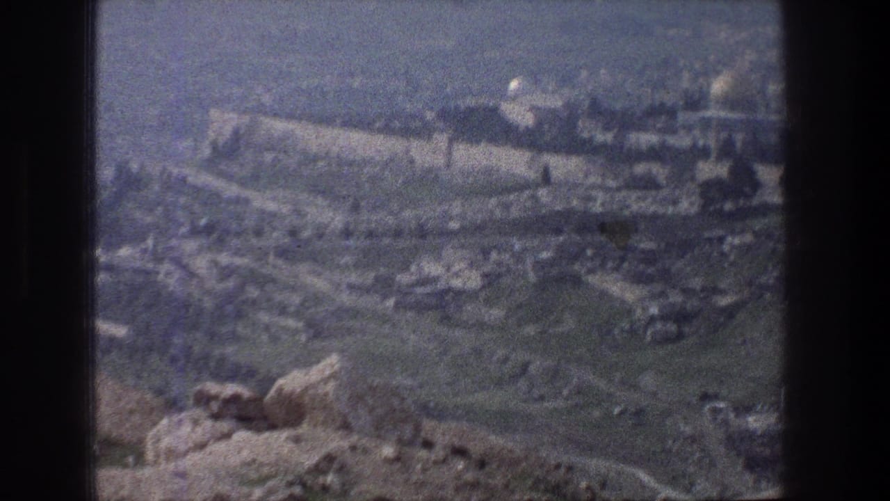 1976 8mm view from a rocky Jerusalem overlook toward the old city walls and distant domes under a soft blue cast.