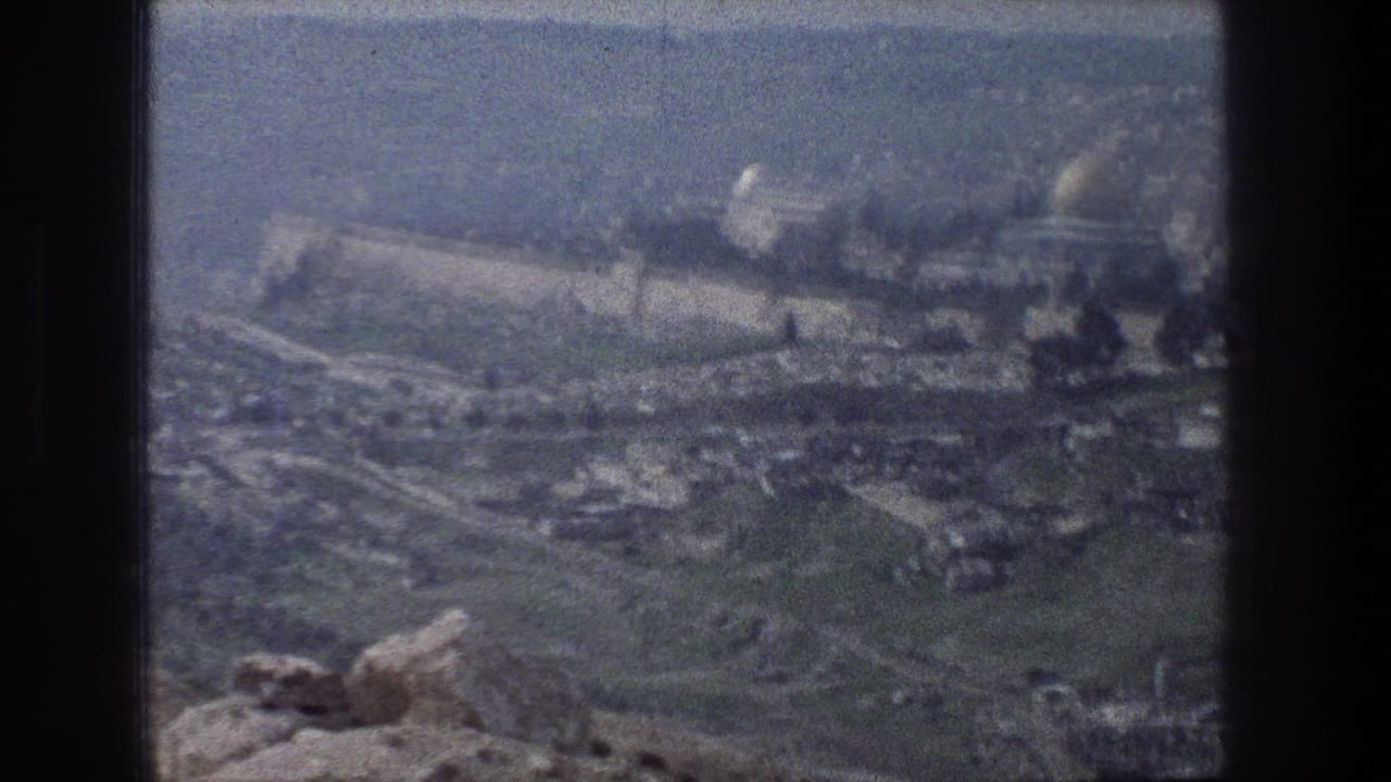 Wide 1976 Jerusalem travel frame showing foreground rocks, the old city wall, distant domes, and soft grain from 8mm film.