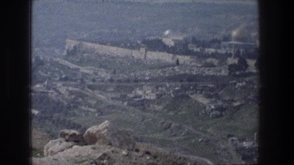 Jerusalem in 1976 seen from a visitor overlook, with rocky ground, hillside roads, old walls, and domes softened by faded 8mm color.