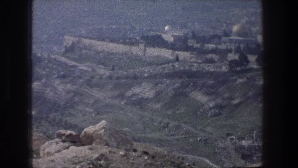 Faded 1976 8mm frame looking across Jerusalem's rocky hills toward the walled city and domed religious architecture.