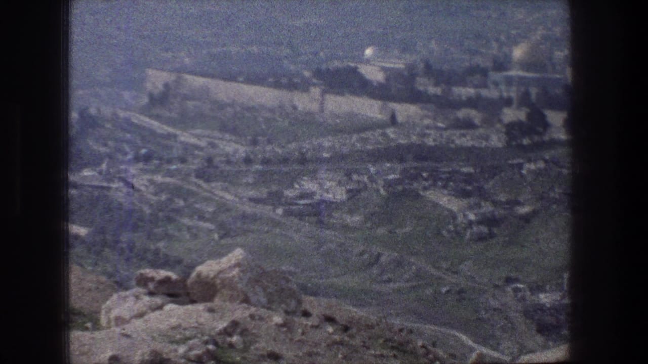 1976 8mm view from above Jerusalem, showing rocky foreground, green slopes, and ancient stone walls in the distance.