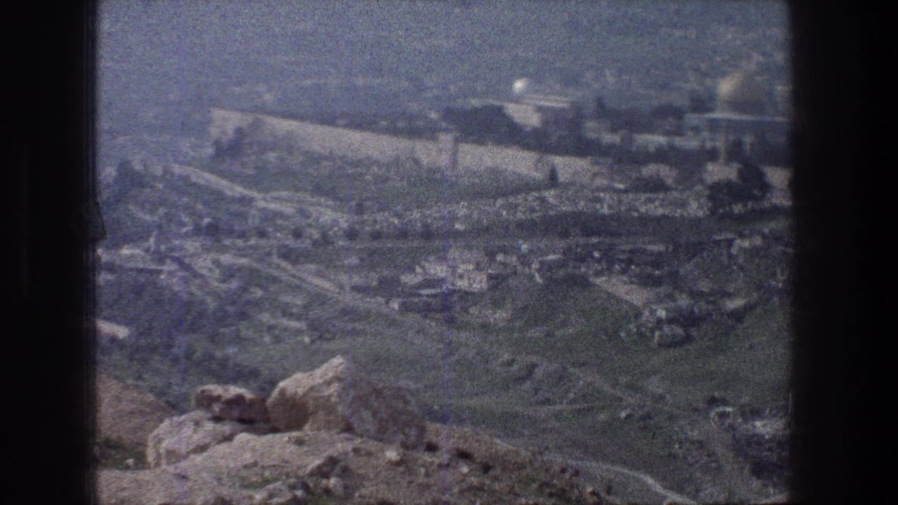1976 home-movie frame of Jerusalem from an overlook, with stone walls, scattered greenery, and distant structures.