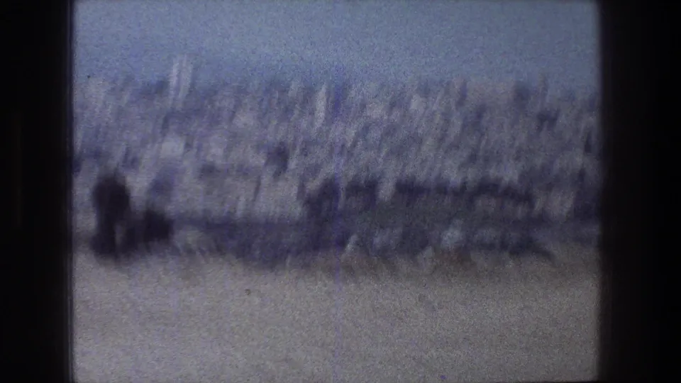 Blue-tinted, motion-softened 1976 Jerusalem-area frame showing a distant built hillside and open terrain.