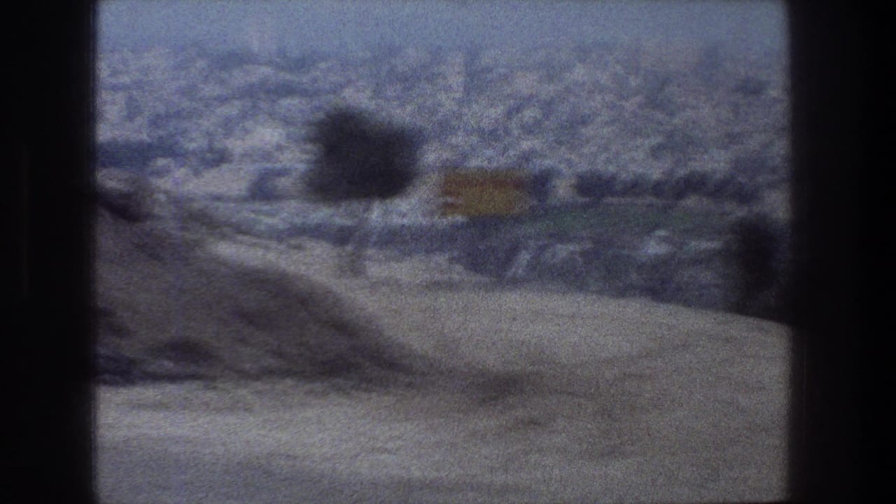 Blurred city hills and a roadside sign or object seen through a vehicle window.