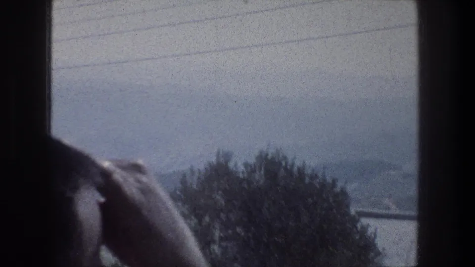 A 1976 Jerusalem travel shot shows power lines, foreground trees, and distant hills from inside a moving vehicle.