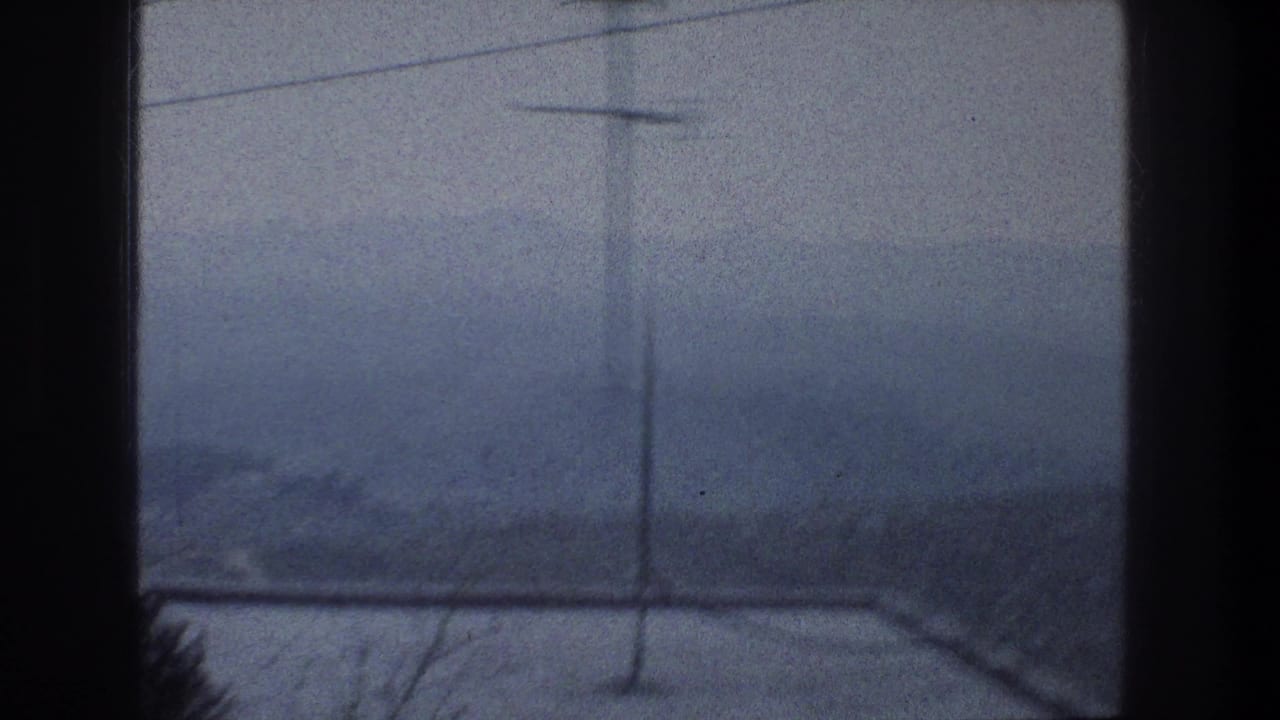 Window-framed view of a misty hillside with antennas and roofline shapes.
