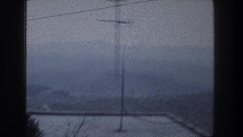 1976 Jerusalem view through a dark window frame, with a misty hillside, antenna lines, and faint urban forms beyond.