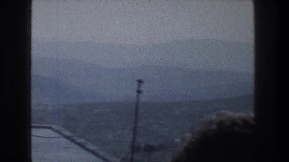 1976 Jerusalem window view with rooftop line, antenna, distant hillside, and a partial dark head silhouette at the lower right.
