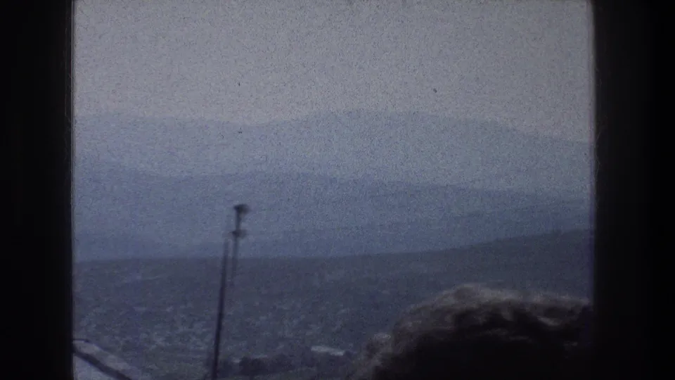1976 8mm Jerusalem view through a window, showing haze over distant buildings and hills with a silhouetted head low in frame.