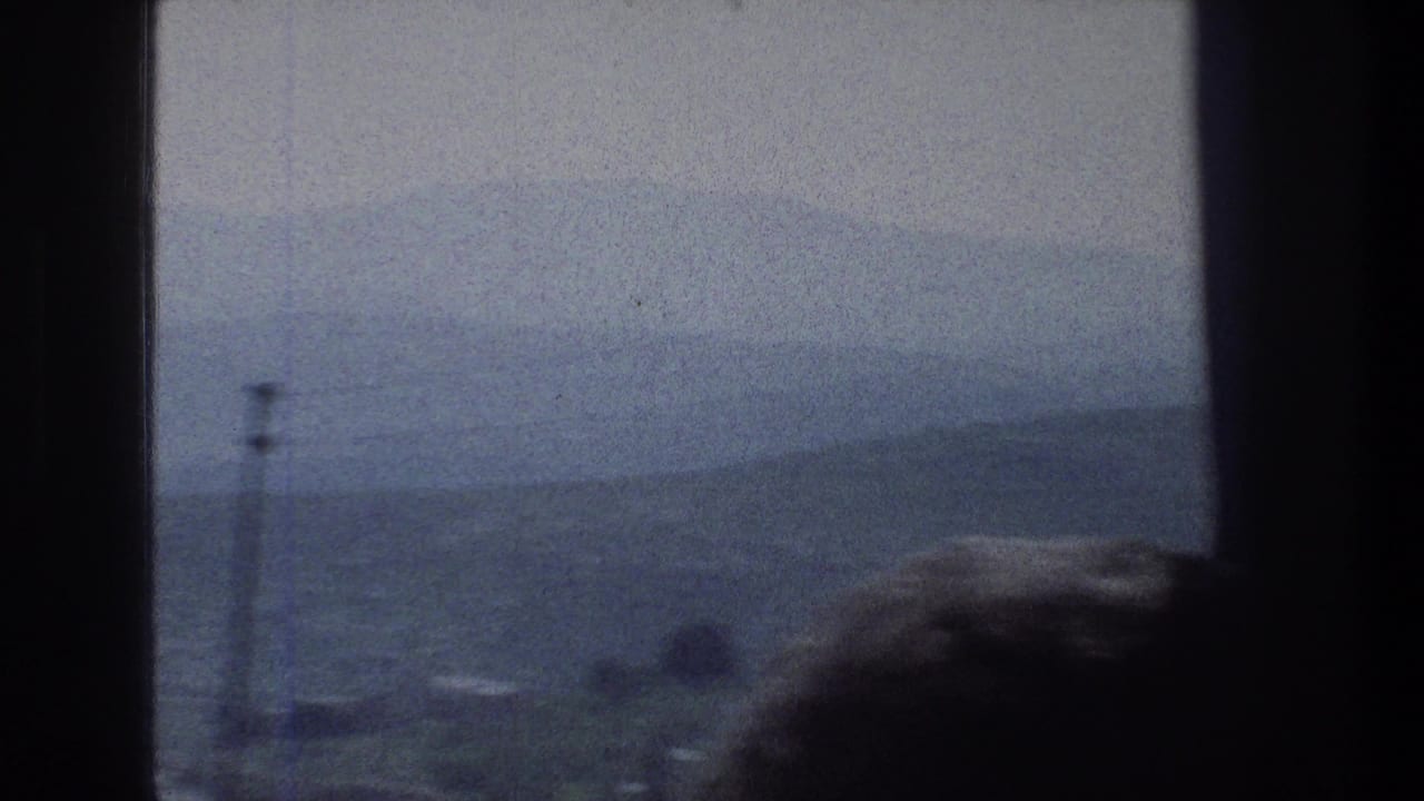 Window-framed hazy hillside view with a tall pole and a dark head shape in the foreground.